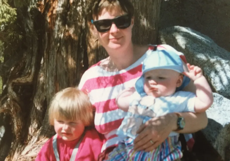 Susan in a striped top sitting on rocks with her two young children