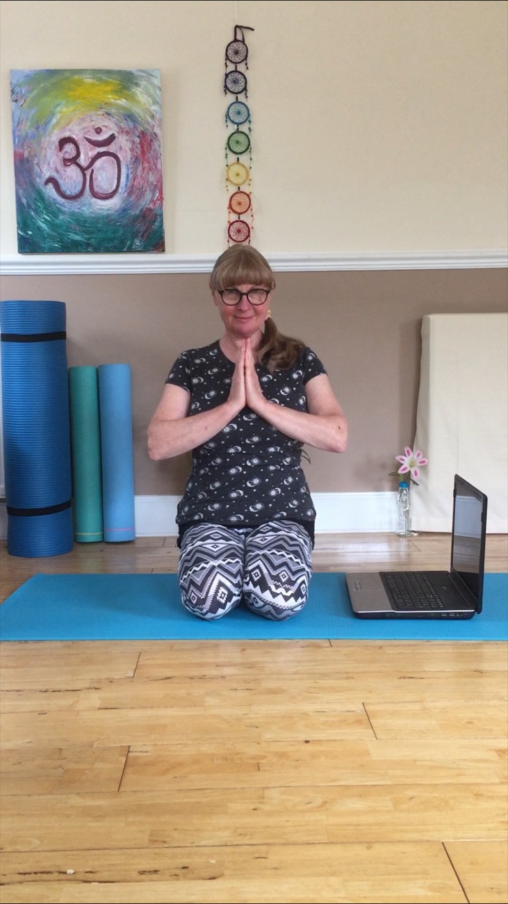 Susan sitting cross-legged on her mat with her hands together