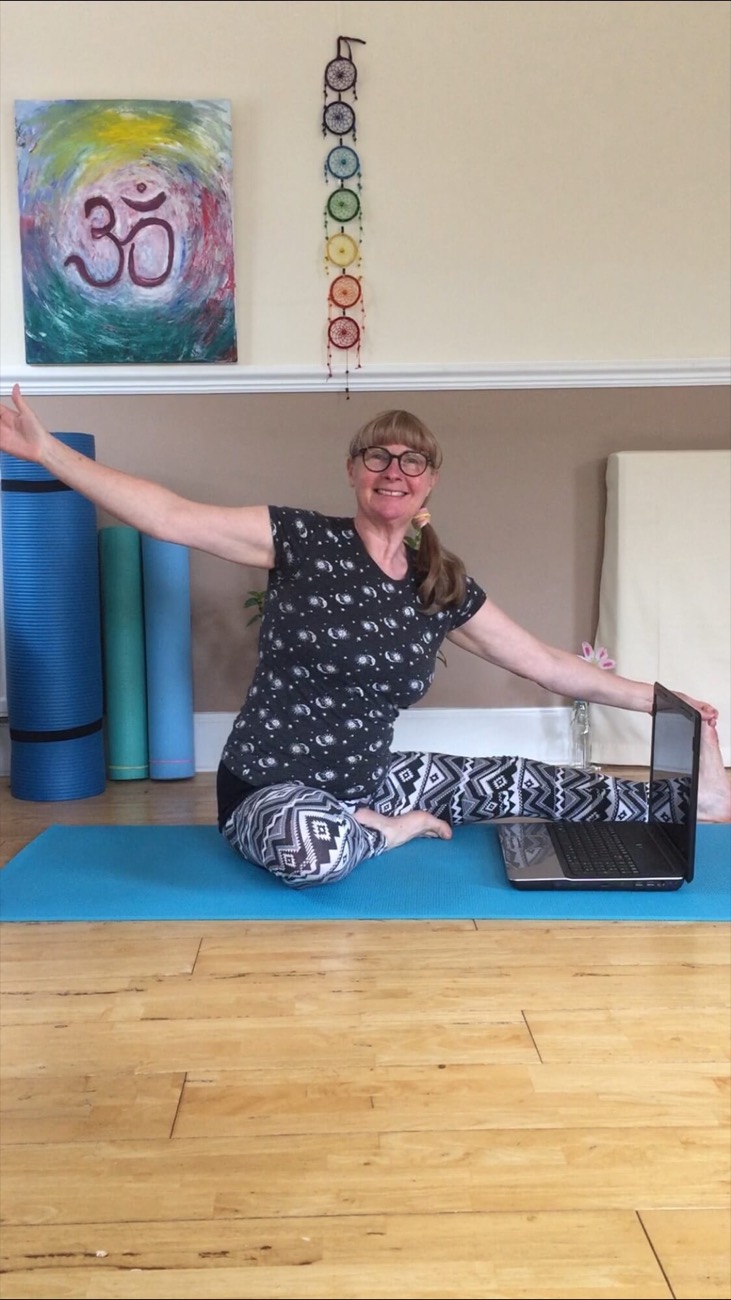 Susan seated on her mat with arms stretched wide, smiling