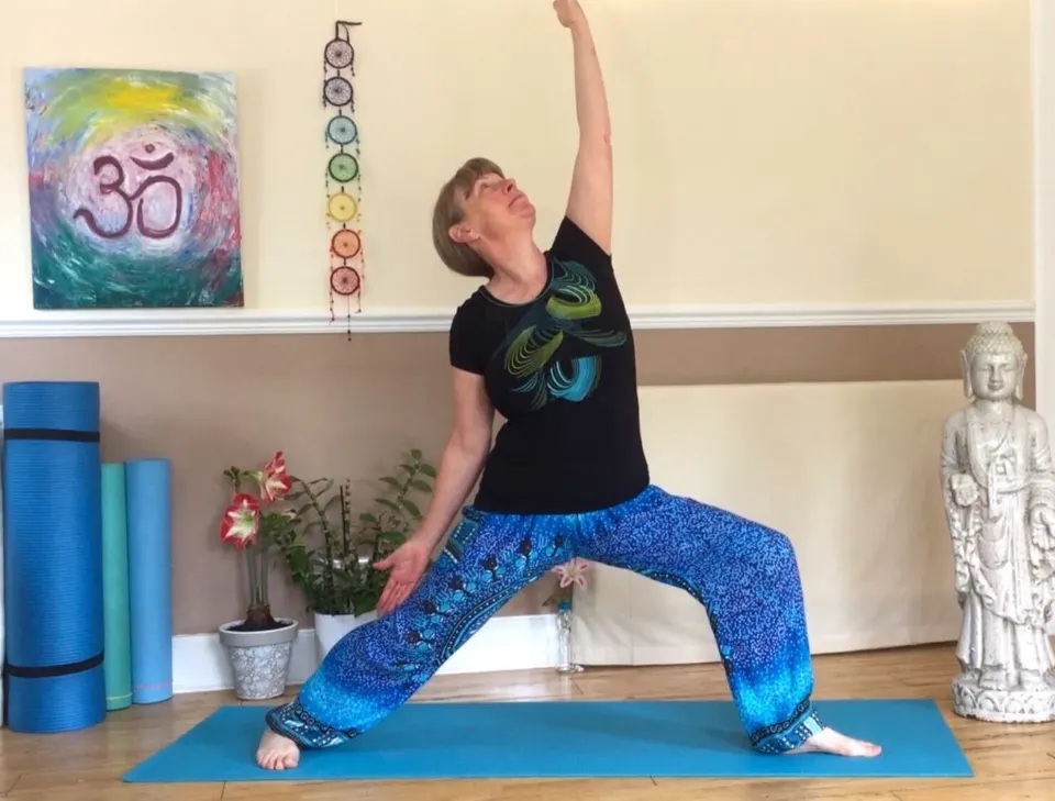 Susan in a reaching warrior pose in her yoga room