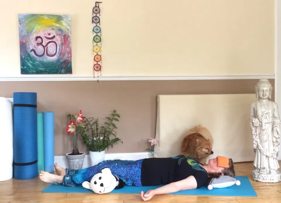 Susan resting in Yoga Nidra on her mat, a cushion under her head and a soft toy beside her